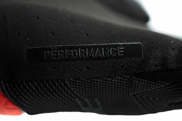 Nahaufnahme der schwarzen, strukturierten Oberfläche der CUBE Handschuhe Performance langfinger X Actionteam, mit geprägtem Wort PERFORMANCE und roten sowie gemusterten schwarzen Details., Ansicht 3