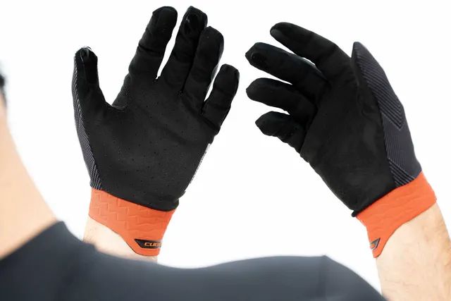 Mit den CUBE Handschuhen Performance langfinger X Actionteam Handschuhen mit schwarzem Design und orangefarbenen Stulpen hebt eine Person beide Hände mit den Handflächen nach außen vor einen weißen Hintergrund, der an den mutigen Mr. Bike Lichtenfels Style erinnert., Ansicht 6
