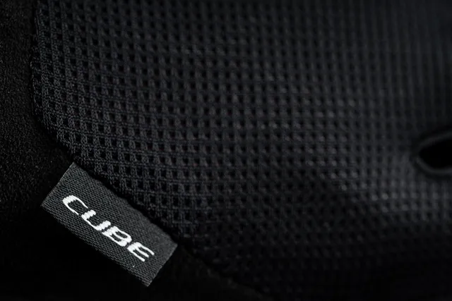 Nahaufnahme des schwarz strukturierten Mesh-Gewebes der CUBE Handschuhe langfinger X NF, mit einem kleinen Stoffanhänger mit "CUBE" in weißen Buchstaben. Vorgestellt bei Mr. Bike Lichtenfels., Ansicht 3