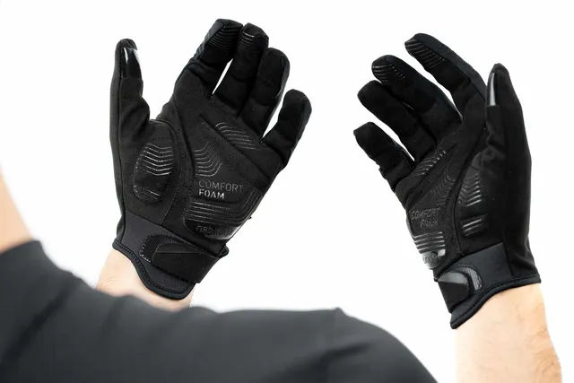 Eine Person trägt CUBE Handschuhe langfinger X NF schwarz gepolsterte Handschuhe mit erhobenen Händen vor einem weißen Hintergrund. Die Handschuhe haben verstärkte Bereiche und strukturierte Griffe an den Handflächen und Fingern., Ansicht 6