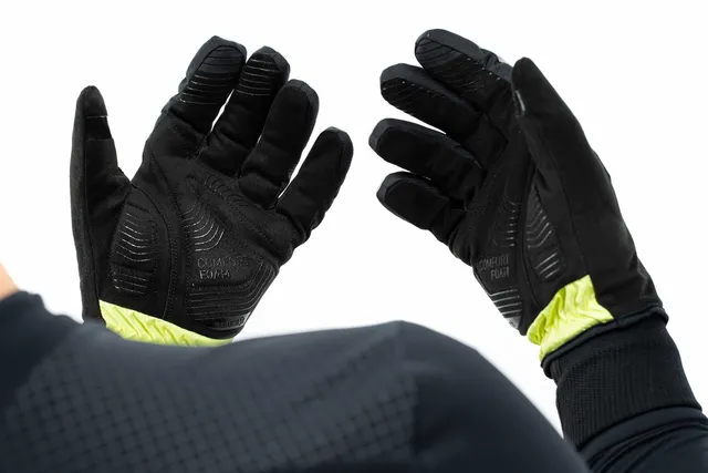 Eine Person, die schwarze CUBE Handschuhe Winter langfinger X NF mit strukturierten Griffen und gelben Handflächenakzenten trägt, hebt beide Hände vor einem weißen Hintergrund., Ansicht 6