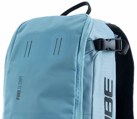 Nahaufnahme eines hellblauen CUBE Rucksack PURE 12 CMPT mit schwarzen Trägern und Schnallen, "PURE 12 CMPT" vertikal auf der Vorderseite aufgedruckt. Der strapazierfähige Stoff und die minimalistischen Designdetails stechen hervor., Ansicht 2