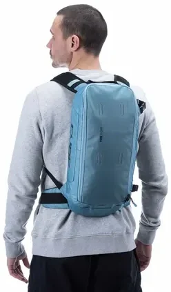 Ein Mann in einem hellgrauen Sweatshirt und einer schwarzen Hose steht mit dem Rücken zur Kamera und präsentiert einen CUBE Rucksack PURE 12 CMPT in Hellblau mit schwarzen Trägern vor einem schlichten weißen Hintergrund., Ansicht 3