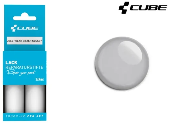 Das CUBE Lackstift Set POLAR SILBER glänzend 2266, abgebildet in blauer Verpackung neben einem passenden silbernen Lackmuster, ist perfekt für Mr. Bike Lichtenfels Fans. Das CUBE-Logo befindet sich in der rechten oberen Ecke.