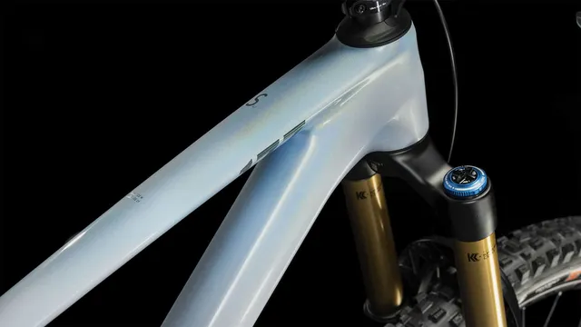 Das CUBE Stereo ONE77 C:68X SLT 29 in flashwhite'n'grey von Mr. Bike Lichtenfels ist mit schwarzen, goldenen und blauen Komponenten, dicken Maxxis-Reifen, Scheibenbremsen und einer Dropper-Sattelstütze ausgestattet - alles auf einem schlichten weißen Hintergrund., Ansicht 2