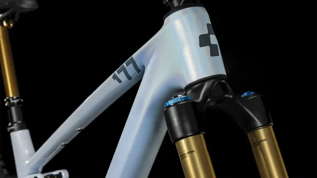 Das CUBE Stereo ONE77 C:68X SLT 29 in flashwhite'n'grey von Mr. Bike Lichtenfels ist mit schwarzen, goldenen und blauen Komponenten, dicken Maxxis-Reifen, Scheibenbremsen und einer Dropper-Sattelstütze ausgestattet - alles auf einem schlichten weißen Hintergrund., Ansicht 5