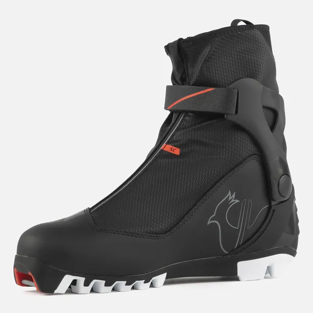 Der ROSSIGNOL X-6 SC ist ein schwarzer Langlaufschuh mit Reißverschluss, roten Akzenten, Klettverschluss im Knöchelbereich und strukturierter Sohle, mit einem minimalistischen Vogel-Logo an der Seite.