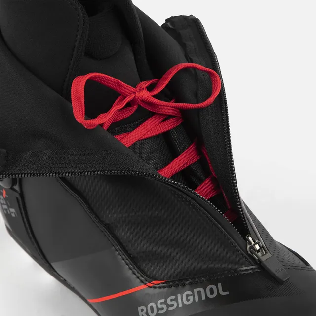 Nahaufnahme des Skischuhs ROSSIGNOL X-6 SC in Schwarz mit roten Schnürsenkeln, teilweise verdeckt durch eine schwarze Außenschicht, die teilweise geöffnet ist. Der Markenname ist an der Seite sichtbar. Erhältlich bei Mr. Bike Lichtenfels.