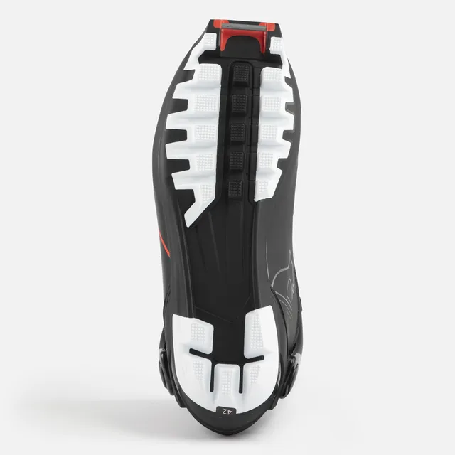 Das Bild zeigt die Sohle eines schwarzen ROSSIGNOL X-6 SKATE Sportschuhs mit weißem und schwarzem Griffmuster, einem Hauch von Rot in der Nähe der Ferse und der Größenangabe 42.