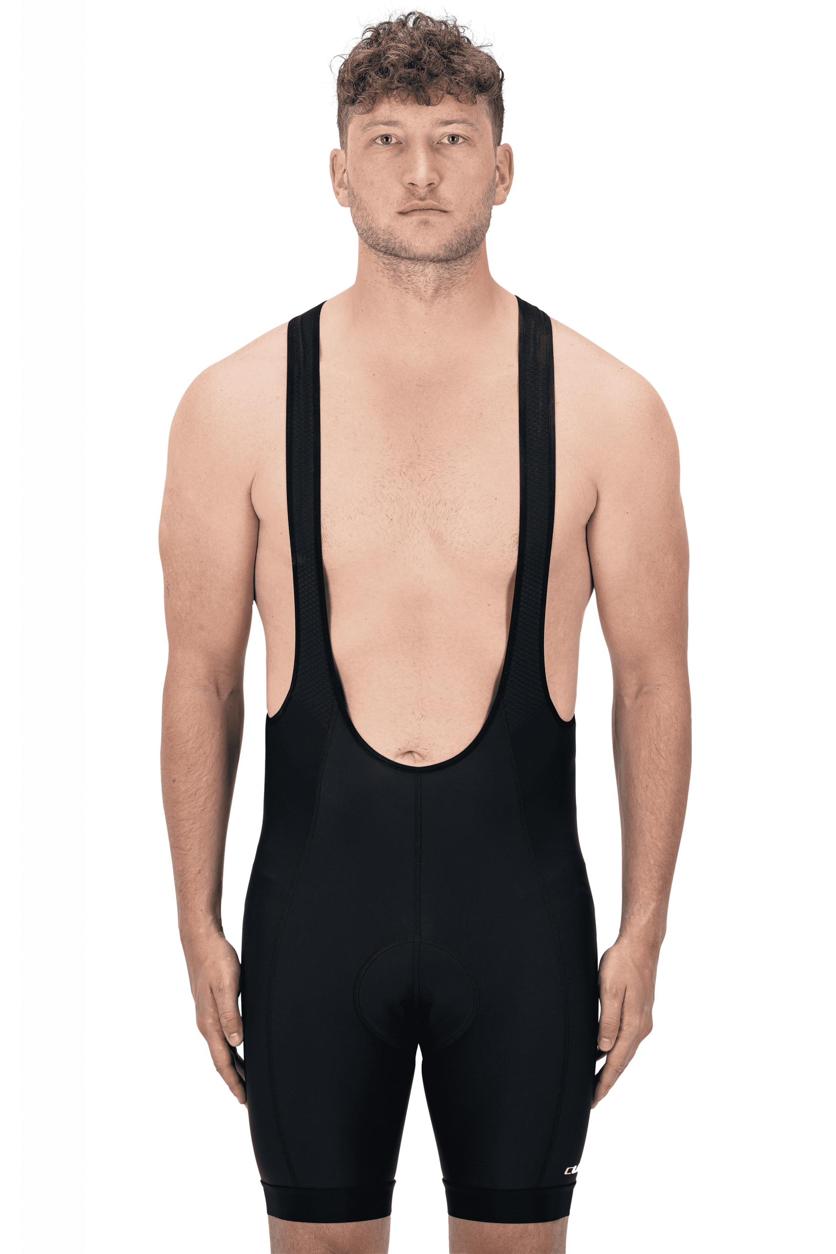 Ein Mann mit kurzen lockigen Haaren und ohne Hemd steht in einer CUBE ATX Trägerhose neben seinem Fahrrad, mit neutralem Gesichtsausdruck auf schlichtem Hintergrund, bereit für eine Fahrt um Lichtenfels.