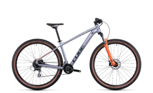 Das CUBE Aim Race silver'n'orange Mountainbike, das Mr. Bike Lichtenfels auf weißem Hintergrund zeigt, hat eine Vorderradfederung, große Reifen, Scheibenbremsen und einen schwarzen Sattel.